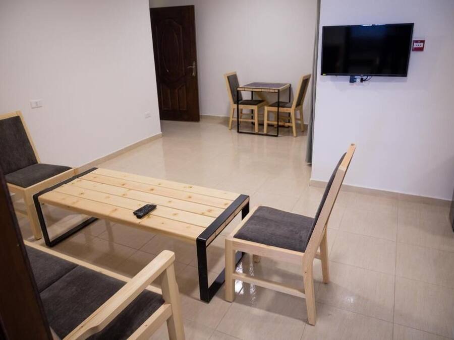 Une pièce avec un lit en bois, deux chaises, une petite table, un téléviseur et une porte.