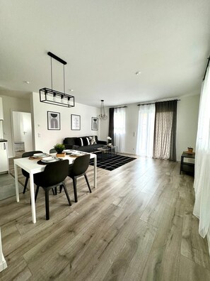 A modern living room with a dining area, a sofa, and a kitchen in the background. - Centrical - Netflix - Queensize Bed (Bruchsal)