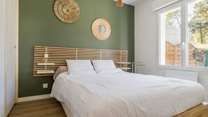 A bedroom with a wooden bed frame, white bedding, and a green wall. There are two wall-mounted circular decorations and a hanging light fixture. - Charming Renovated House Near Beach with Garden & Parking (Saint-Brevin-les-Pins)