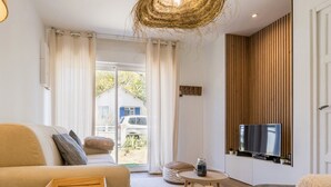 A modern living room with a sofa, a coffee table, and a TV on a wooden wall. - Charming Renovated House Near Beach with Garden & Parking (Saint-Brevin-les-Pins)