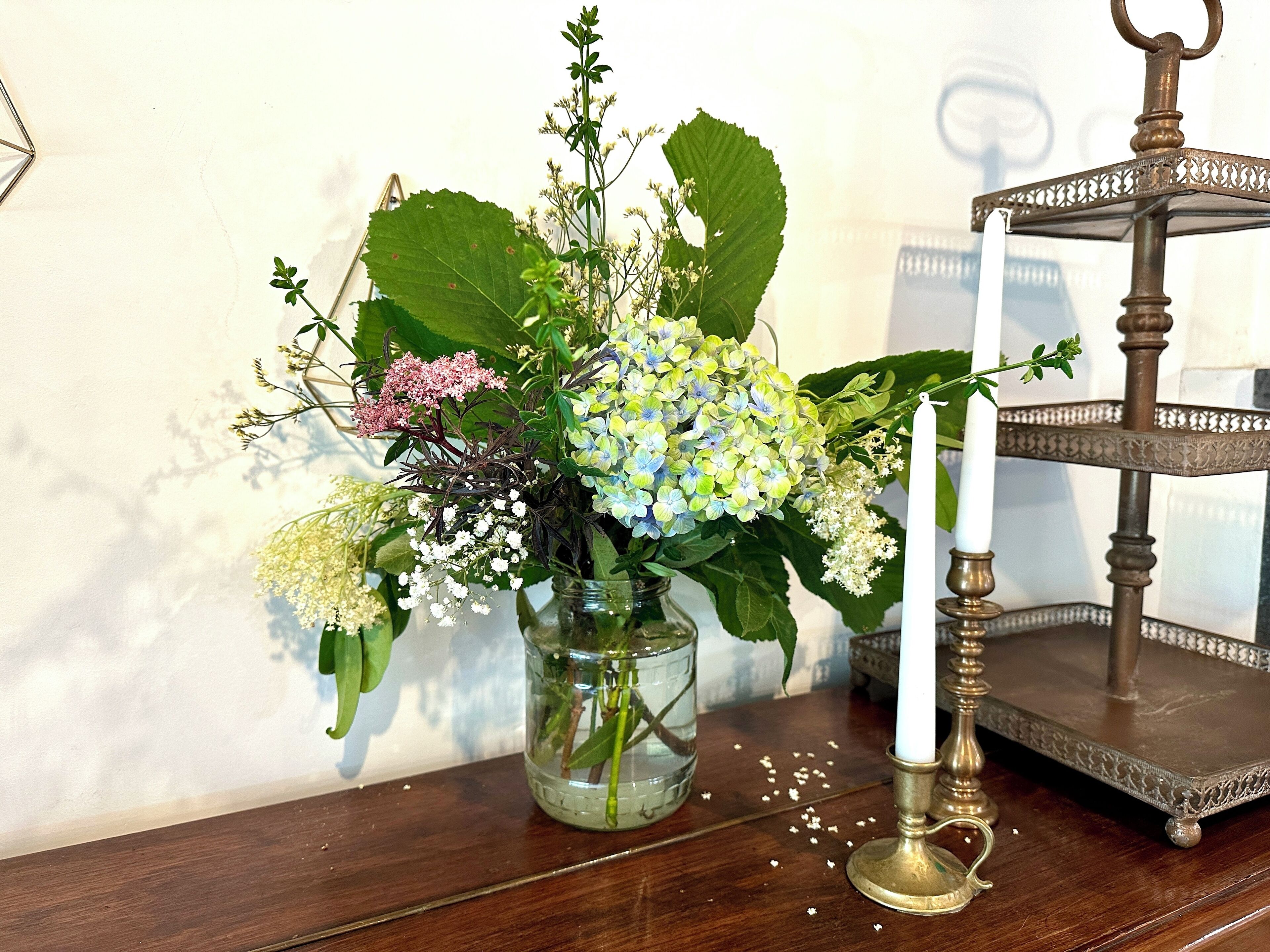 A wooden table with a glass vase containing a floral arrangement, a white candle, and a decorative tray.