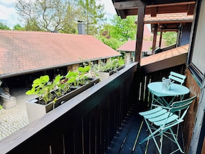 A balcony with a wooden railing, a small table with chairs, and potted plants.