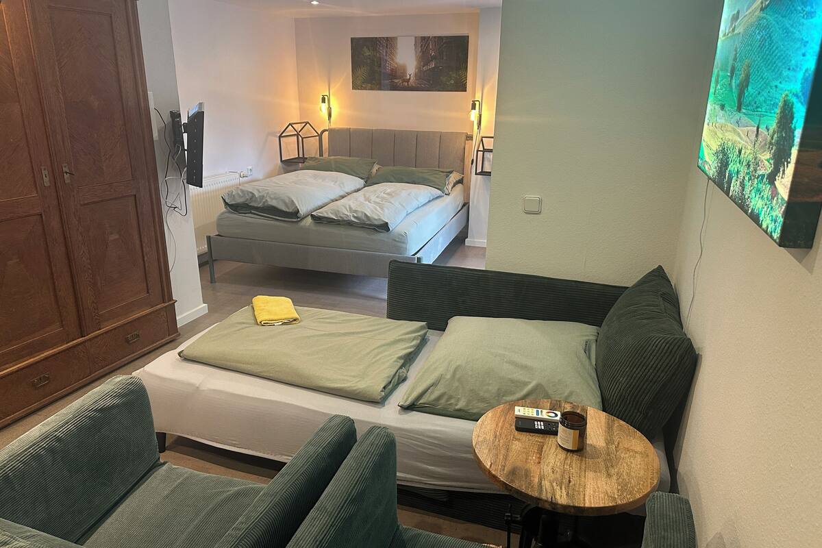 Habitación de hotel con sofá, cama, una pequeña mesa redonda de madera y un cuadro en la pared.