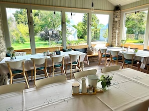 A dining area with tables and chairs, large windows, and a view of a garden.