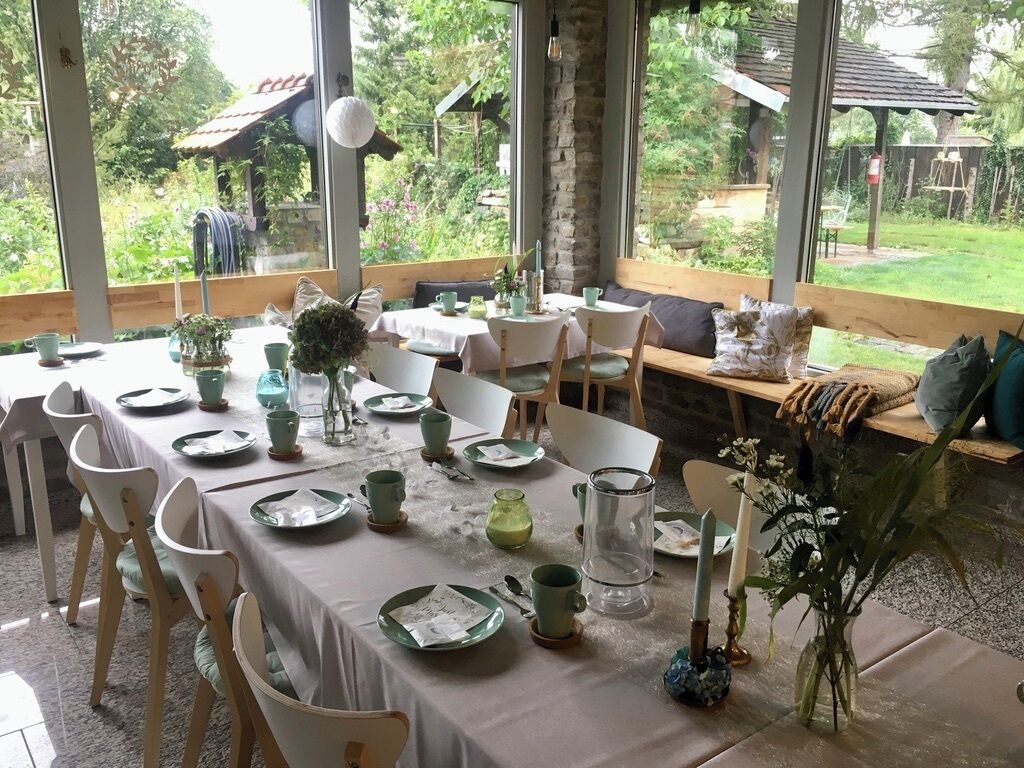 Zona pranzo con tavoli apparecchiati, sedie e vista sul giardino attraverso ampie finestre.