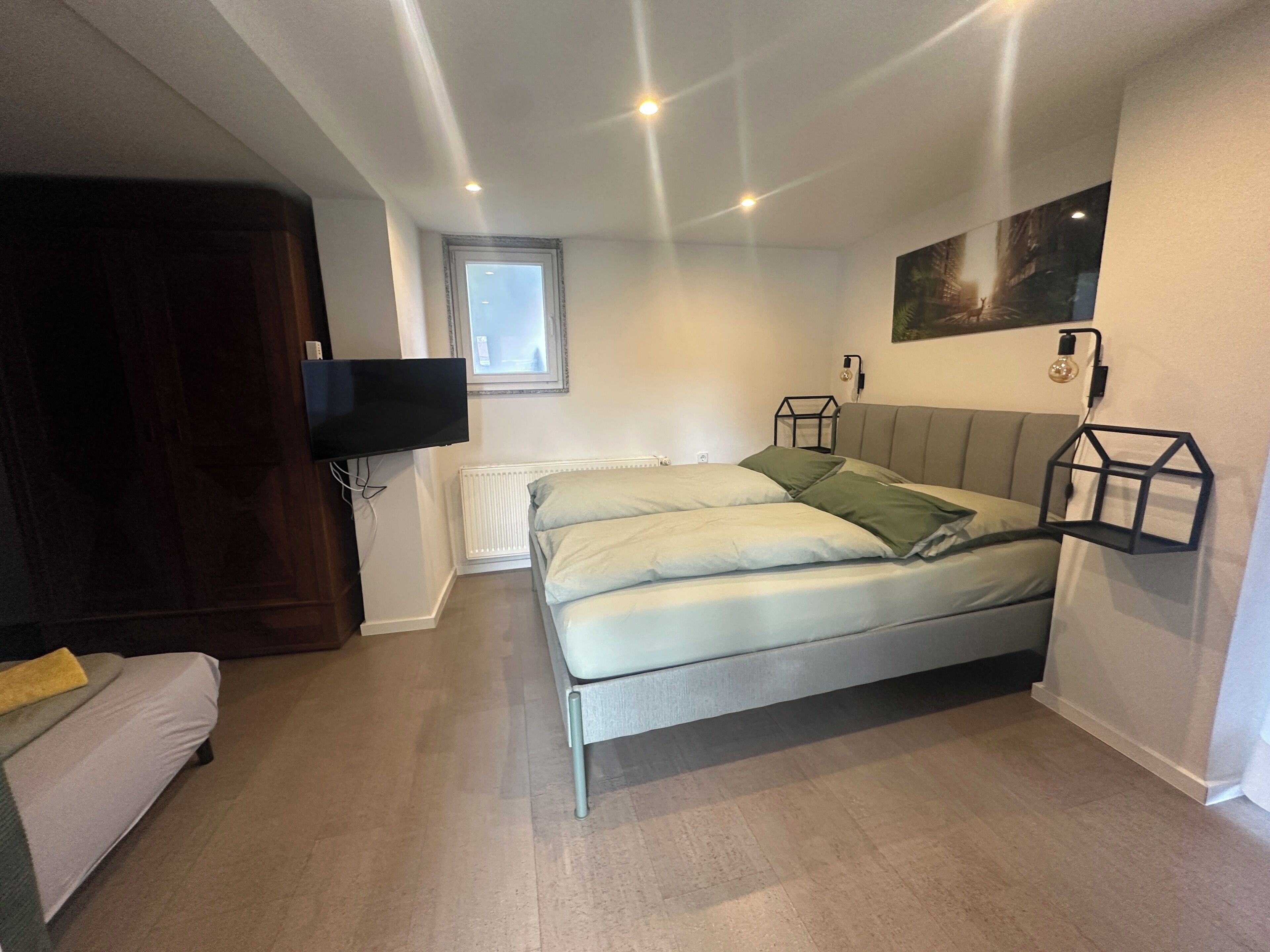 A bedroom with a bed, a TV, a window, a radiator, and a light fixture.