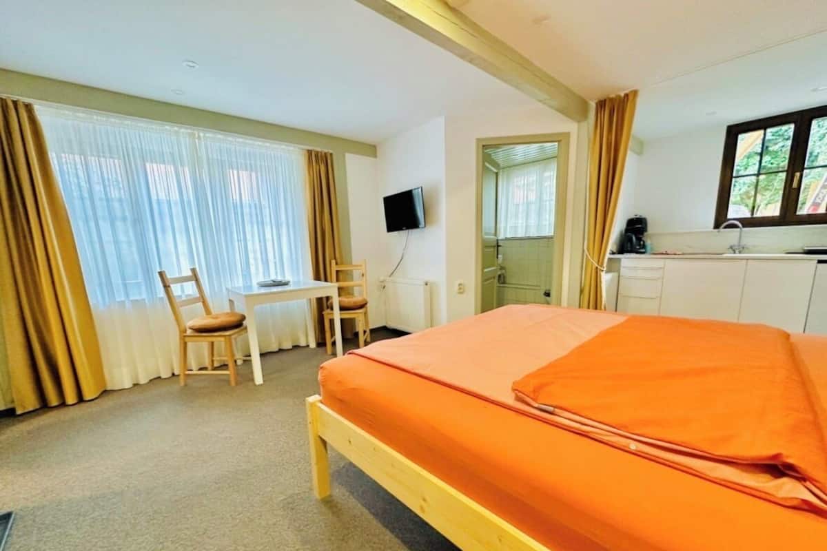 Una habitación de hotel con cama, escritorio, silla, televisión y ventana con cortinas.