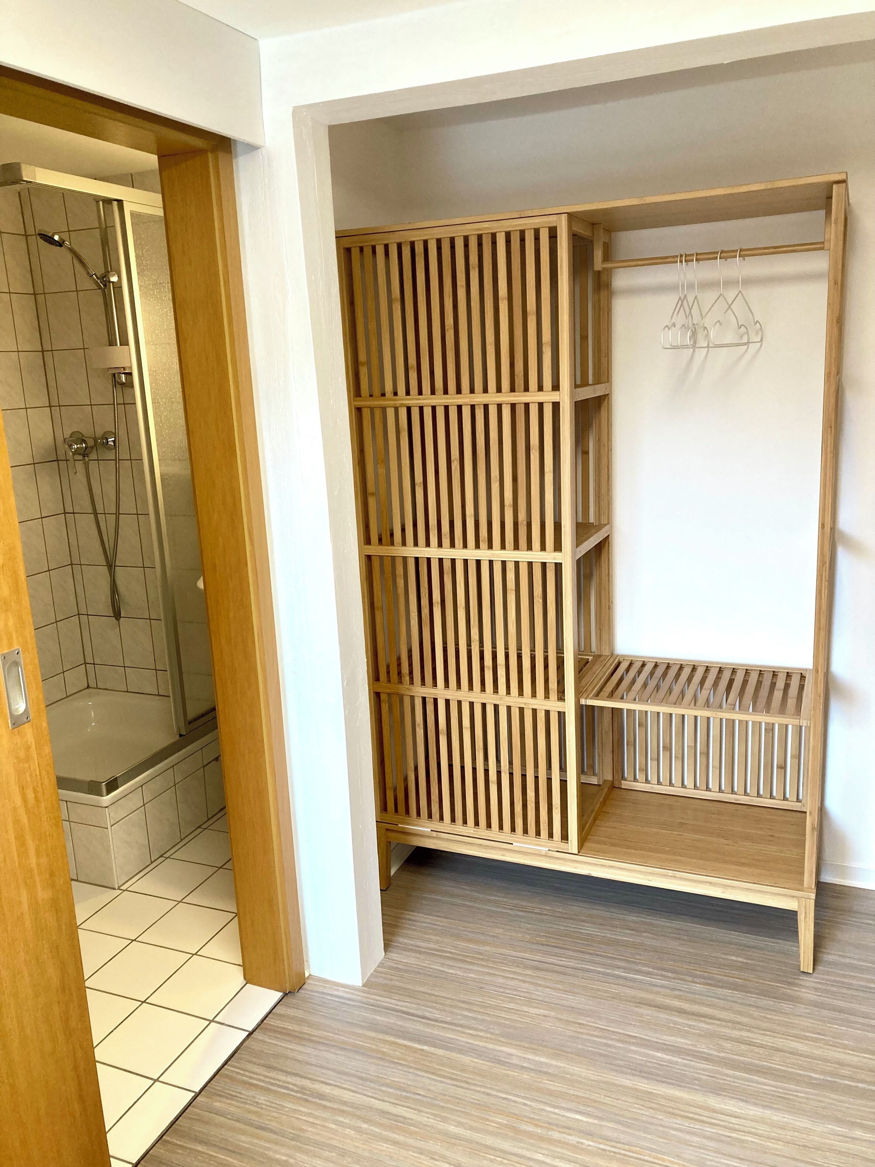 Un dressing accessible sans porte, avec un décor composé de lambris en bois, un espace douche doté d’une porte en verre et un sol carrelé.