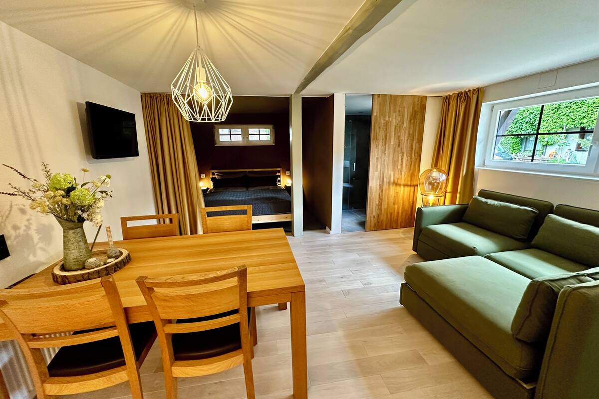 Un espacio habitable moderno con comedor, sofá verde y televisor montado en la pared.