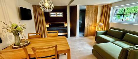 Un espacio habitable moderno con comedor, sofá verde y televisor montado en la pared.
