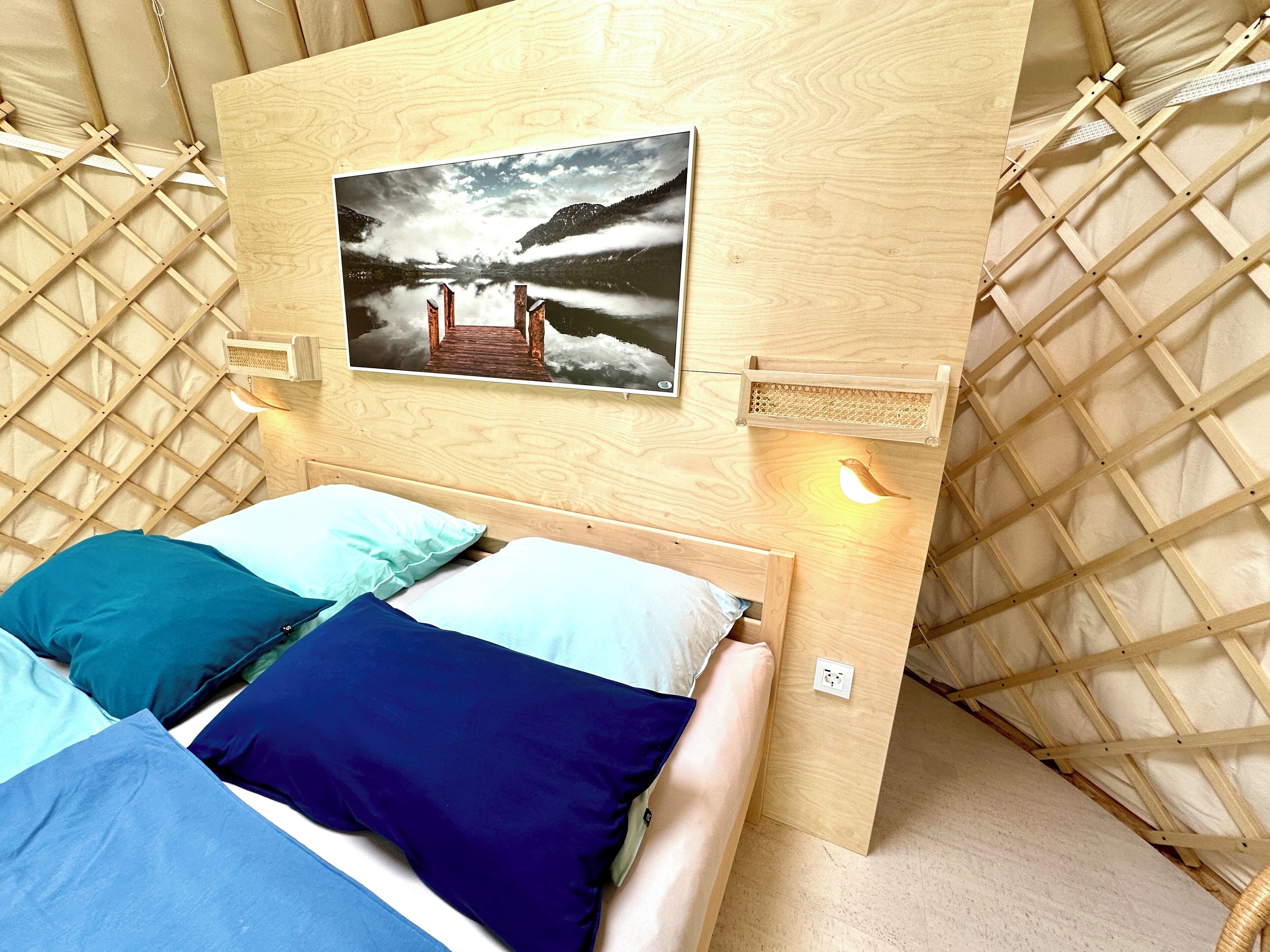 Une chambre chaleureuse avec une tête de lit en bois, un tableau encadré représentant un lac et un lit avec une literie bleue et blanche.