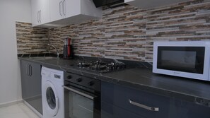 A modern kitchen with a built-in washing machine, a gas stove, and a microwave. - KRABİ APART (Antalya)