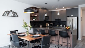 Una cocina moderna con una isla central, sillas negras y una mesa de comedor preparada para seis personas.