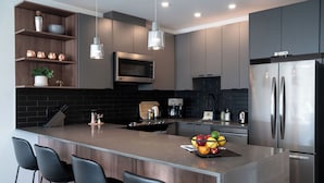 Una cocina moderna con una isla central, taburetes de bar, un refrigerador de acero inoxidable y un microondas.