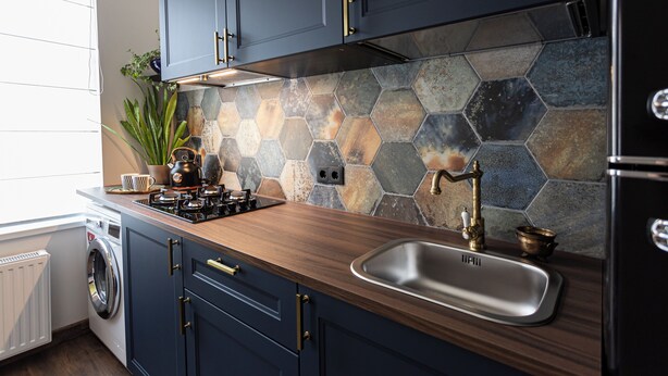 Een moderne keuken met donkerblauwe kastjes, een houten aanrechtblad, een roestvrijstalen spoelbak en een backsplash van hexagonale tegels.