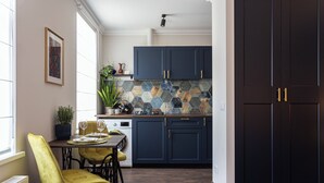 Een moderne keuken met donkerblauwe kastjes, een eethoek met gele stoelen en een groot raam dat zorgt voor natuurlijk licht.