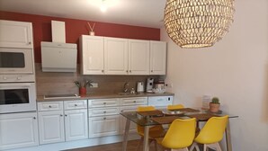 A modern kitchen with white cabinets, a glass dining table with yellow chairs, and a hanging light fixture.