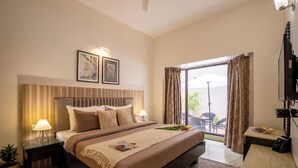 Une chambre d’hôtel avec un grand lit, une table de chevet avec une lampe, une télévision et une vue sur l’extérieur grâce à une porte-fenêtre coulissante.
