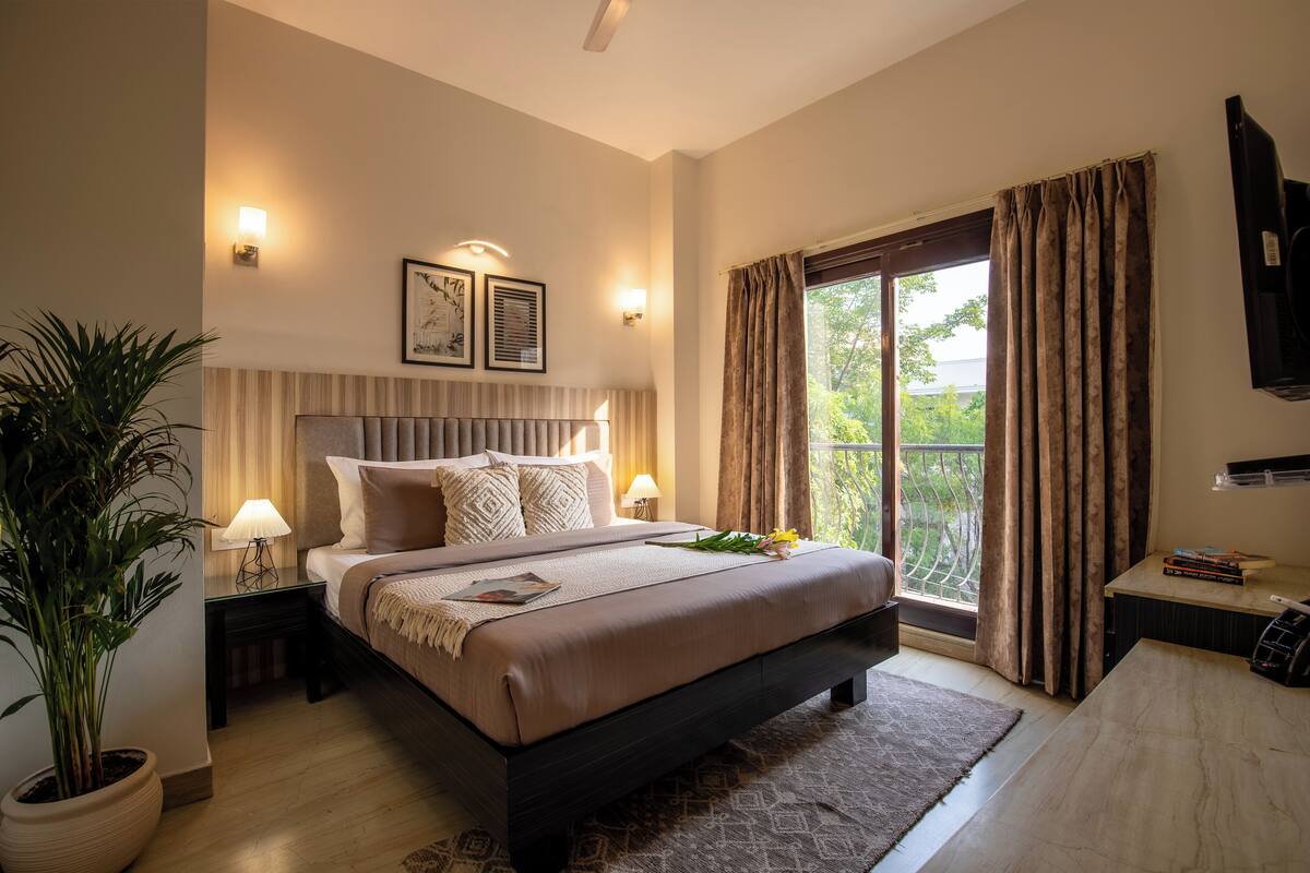 Een moderne hotelkamer met een groot bed, nachtkastjes, een potplant en uitzicht op het omliggende landschap.