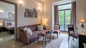 Un salon moderne avec un canapé, un fauteuil et une table basse. On y trouve des tableaux encadrés au mur, une lampe et une fenêtre avec des rideaux.