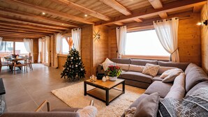 L’intérieur d’un chalet en bois chaleureux et accueillant, avec un coin repas, un salon doté d’un canapé et d’une table basse, et un sapin de Noël.