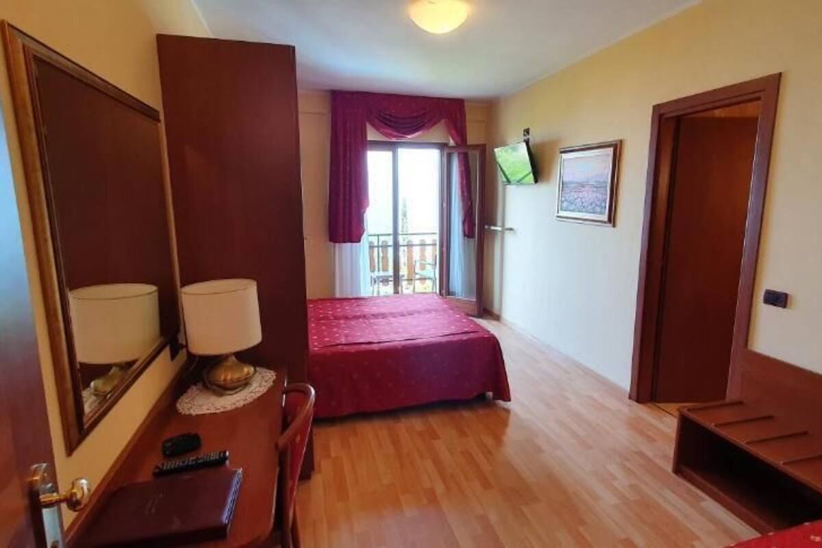 Una habitación con cama, escritorio, silla, lámpara y ventana con cortinas.
