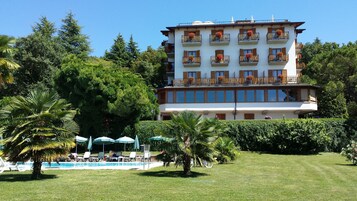 Hotel com vários andares, varandas, piscina e vegetação exuberante.