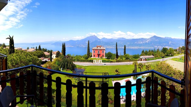 Un balcon avec vue sur un lac, des montagnes et un bâtiment rouge.