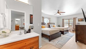Une chambre à coucher avec un lit, des tables de chevet, un ventilateur de plafond et une fenêtre avec des rideaux.