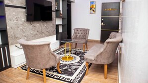 Uma sala de estar moderna com uma TV de tela plana, duas poltronas, uma mesa de centro e um tapete decorativo.