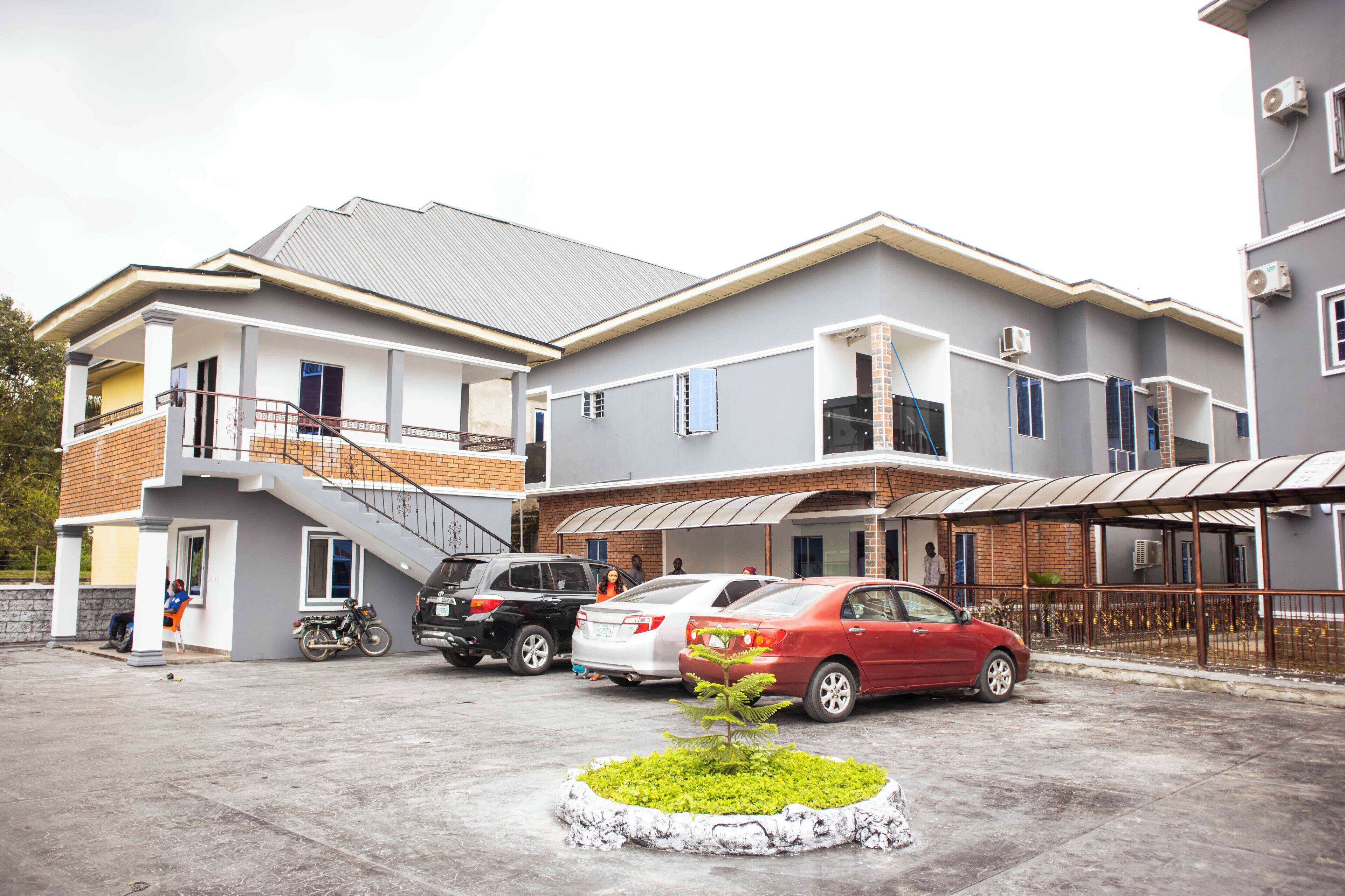 A multi-story residential building with a covered parking area, a small garden, and a staircase leading to the upper floors.