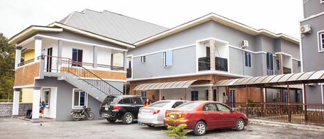 A multi-story residential building with a covered parking area, a small garden, and a staircase leading to the upper floors.