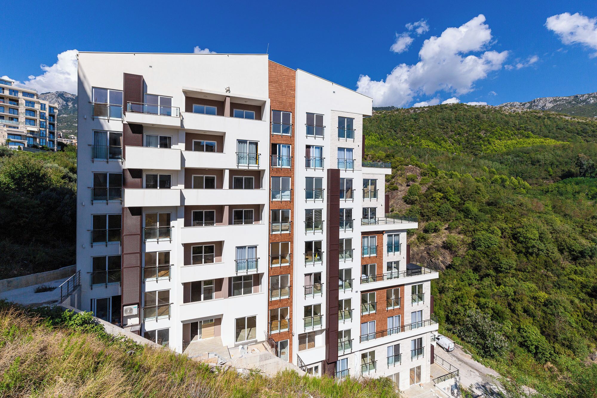 A multi-story hotel with balconies, situated on a hillside with a mountainous backdrop.
