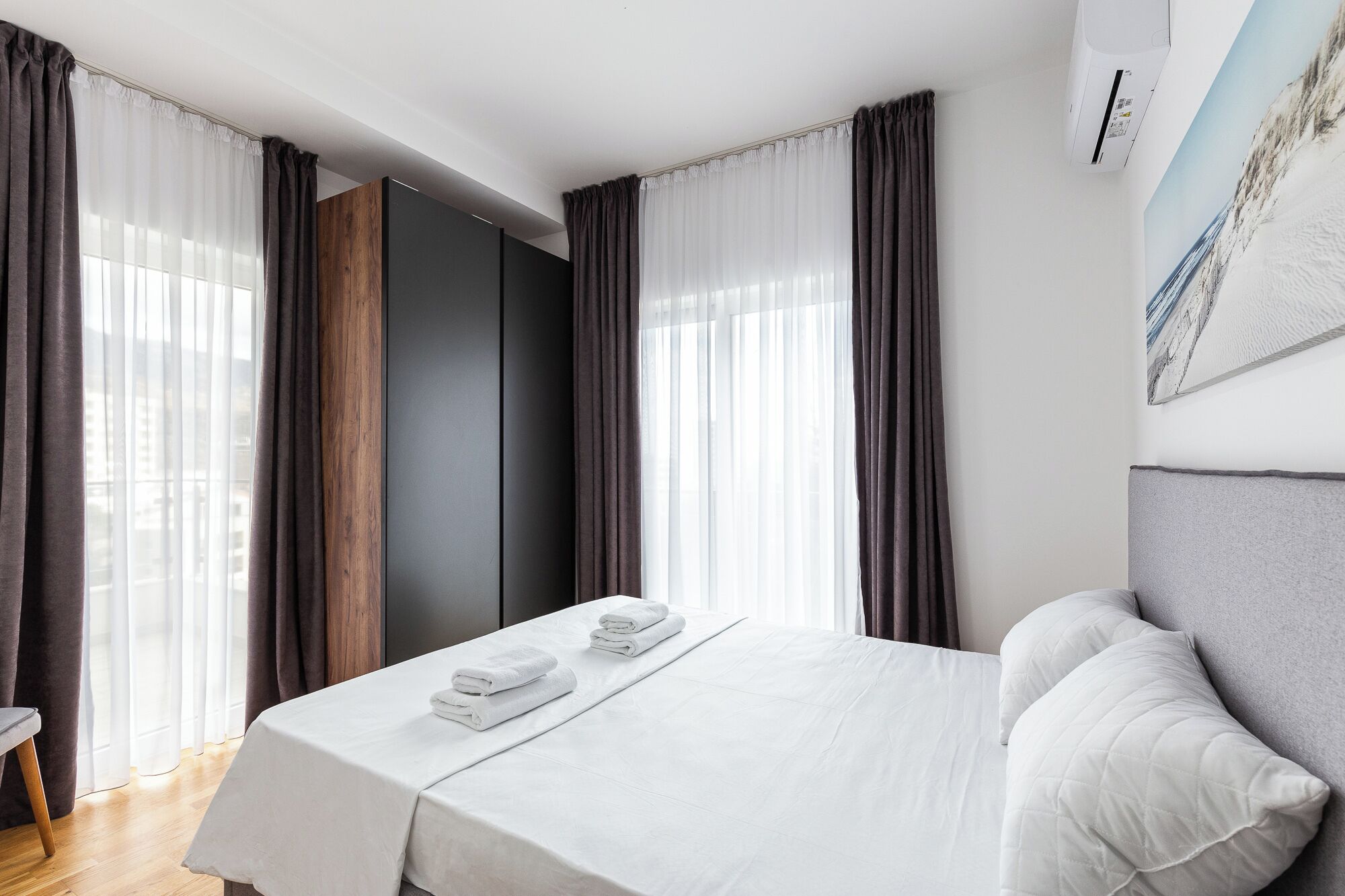 Une chambre d’hôtel moderne avec un grand lit, du linge de lit blanc et une vue sur la ville à travers des rideaux transparents.