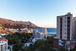 Un paisaje urbano costero con edificios modernos, montañas al fondo y una vista despejada del mar.