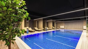 Una piscina interior con agua azul cristalina, rodeada de sillas de descanso y una planta en maceta.
