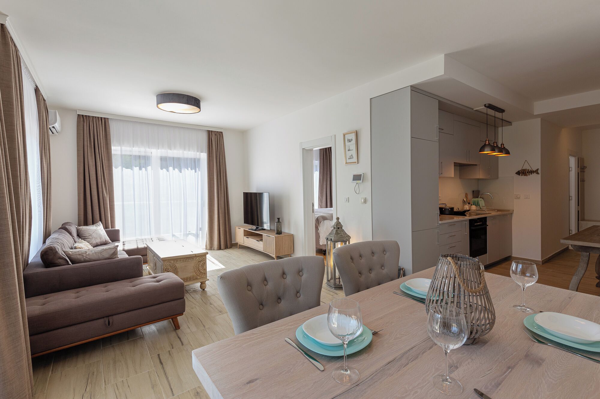 Ein modernes Wohnzimmer mit einer Couch, einem Esstisch für zwei Personen und einer Küchenzeile mit Schränken und Spüle.