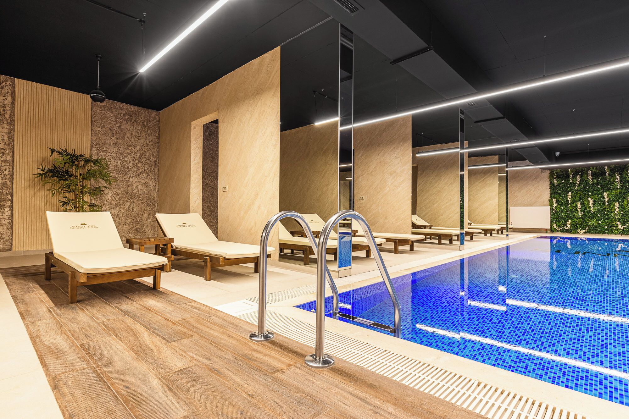 Ein moderner Innenpool mit Holzboden, Liegestühlen und klarem, blauem Wasser.