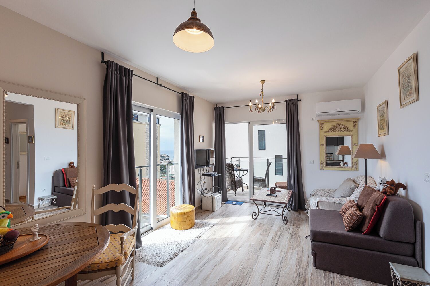 A modern living room with a sofa, a dining table, and a balcony with a view.