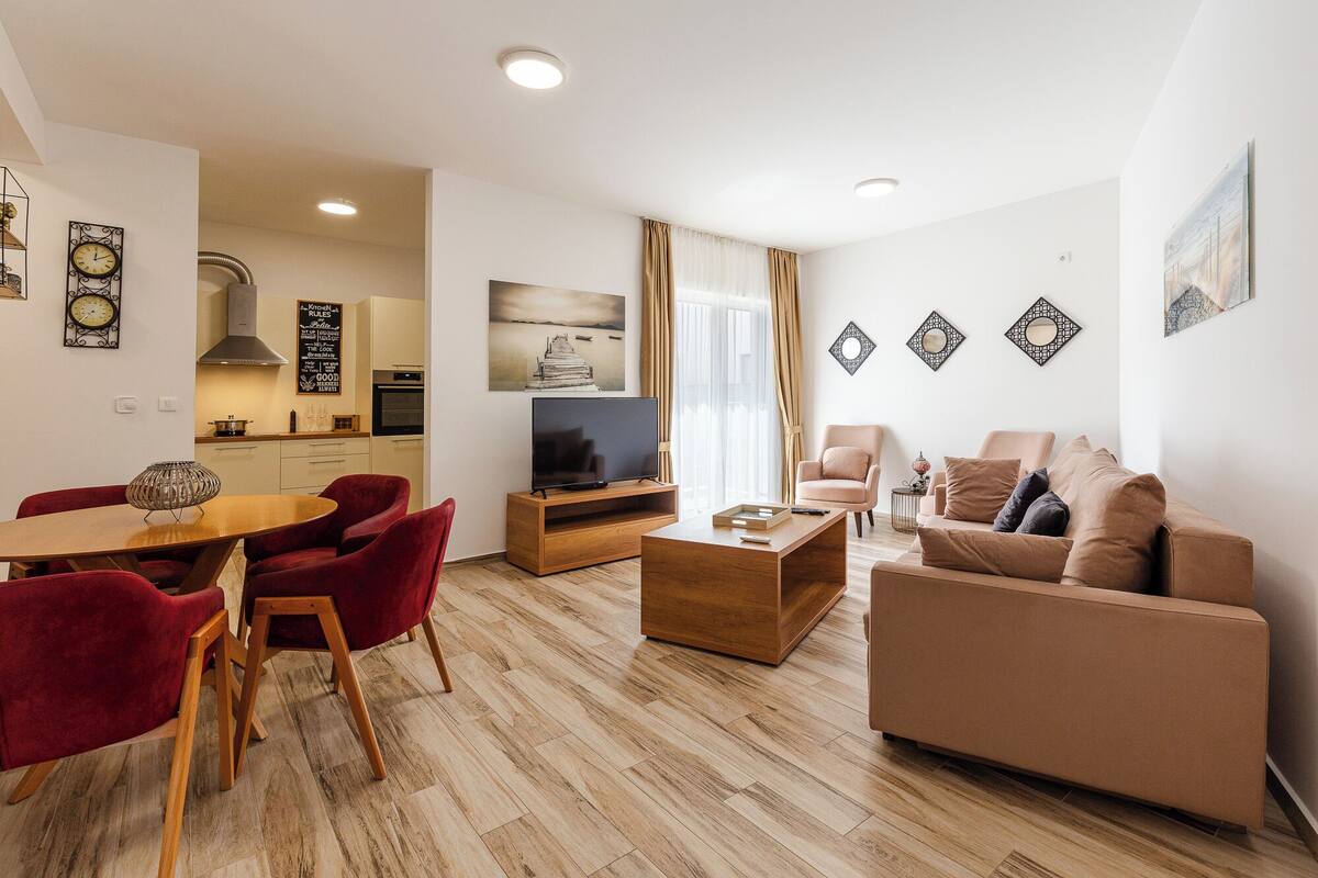 Ein modernes Wohnzimmer mit Fernseher, roten Sesseln, einem beigen Sofa und einem Holztisch.