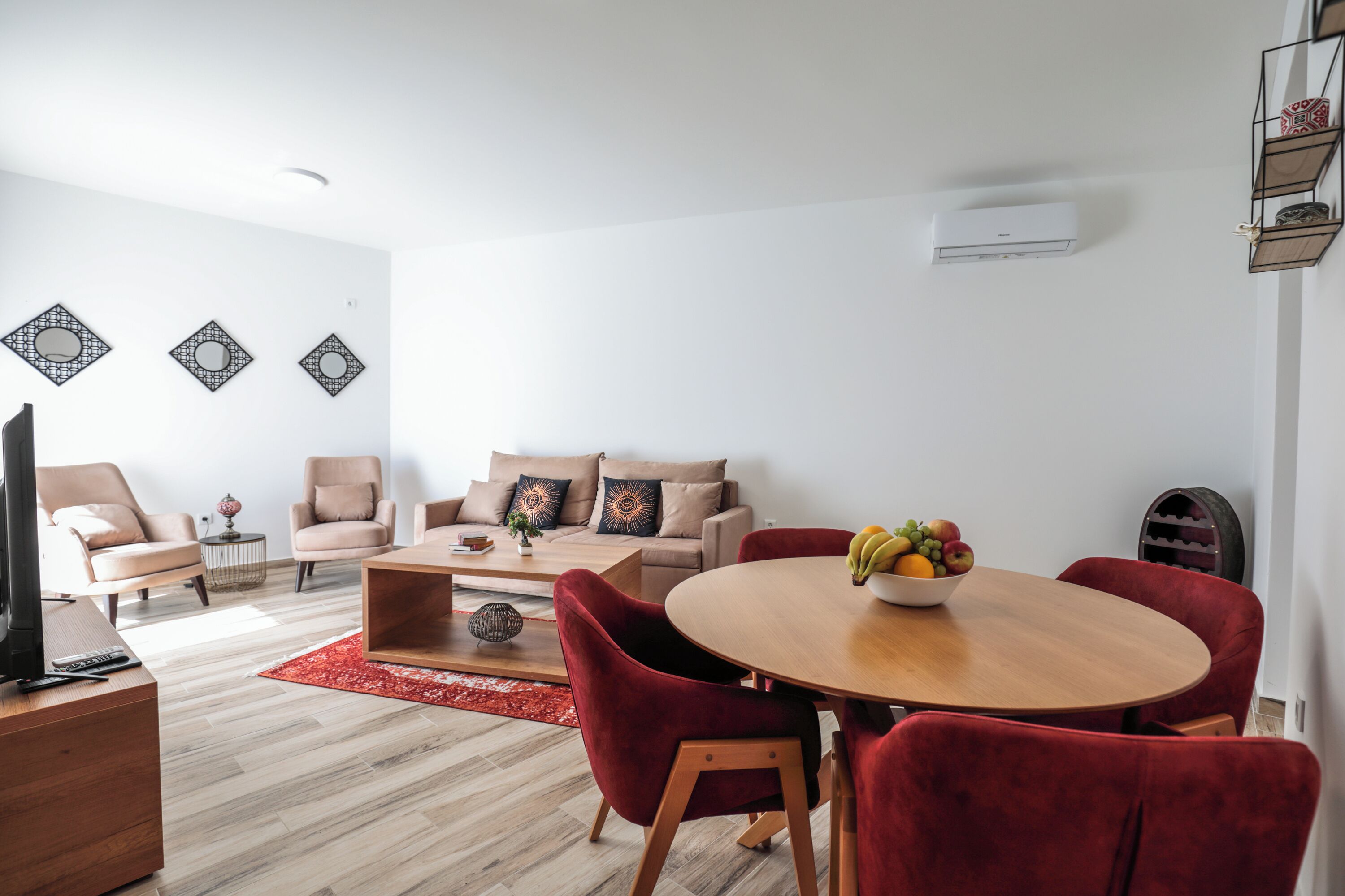 A modern living room with a sofa, red chairs, a wooden coffee table, and a fruit bowl.