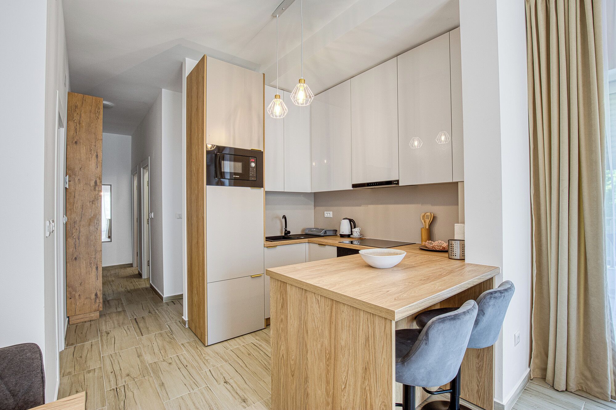 A modern kitchen with a wooden island, bar stools, and pendant lighting.
