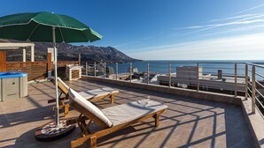 Una terraza en la azotea con una tumbona, una sombrilla verde y vistas al mar y a las montañas.