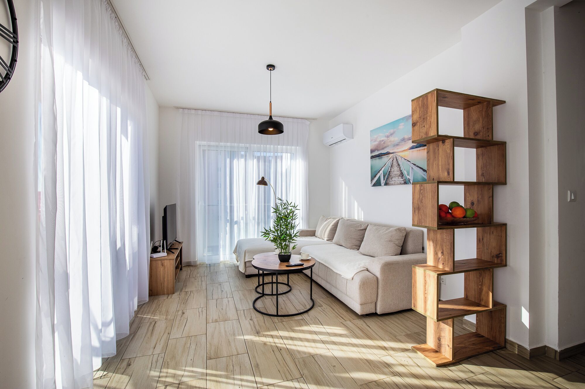 A modern living room with a sofa, a coffee table, a TV, and a wooden shelf unit.