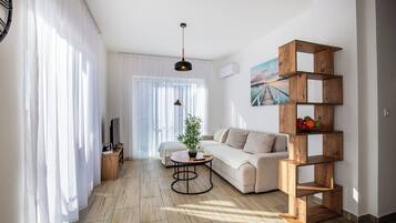 A modern living room with a sofa, a coffee table, a TV, and a wooden shelf unit.
