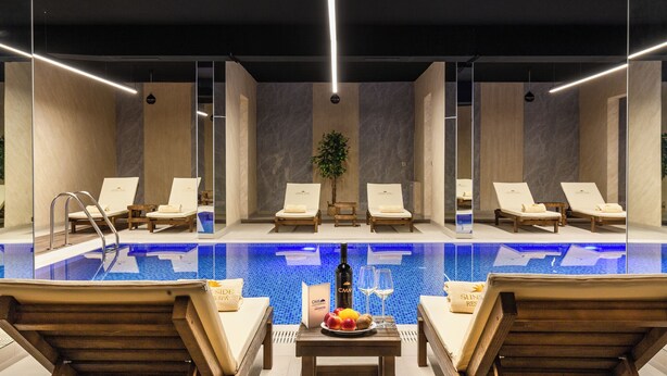 Una piscina interior moderna con sillones de descanso y una mesa con frutas y bebidas.