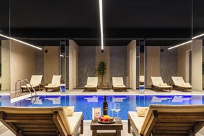 Una piscina interior moderna con sillones de descanso y una mesa con frutas y bebidas.