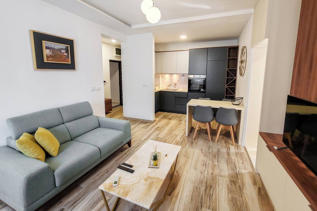 Ein modernes Wohnzimmer mit einem grauen Sofa, einem Couchtisch und einem Essbereich mit Stühlen.