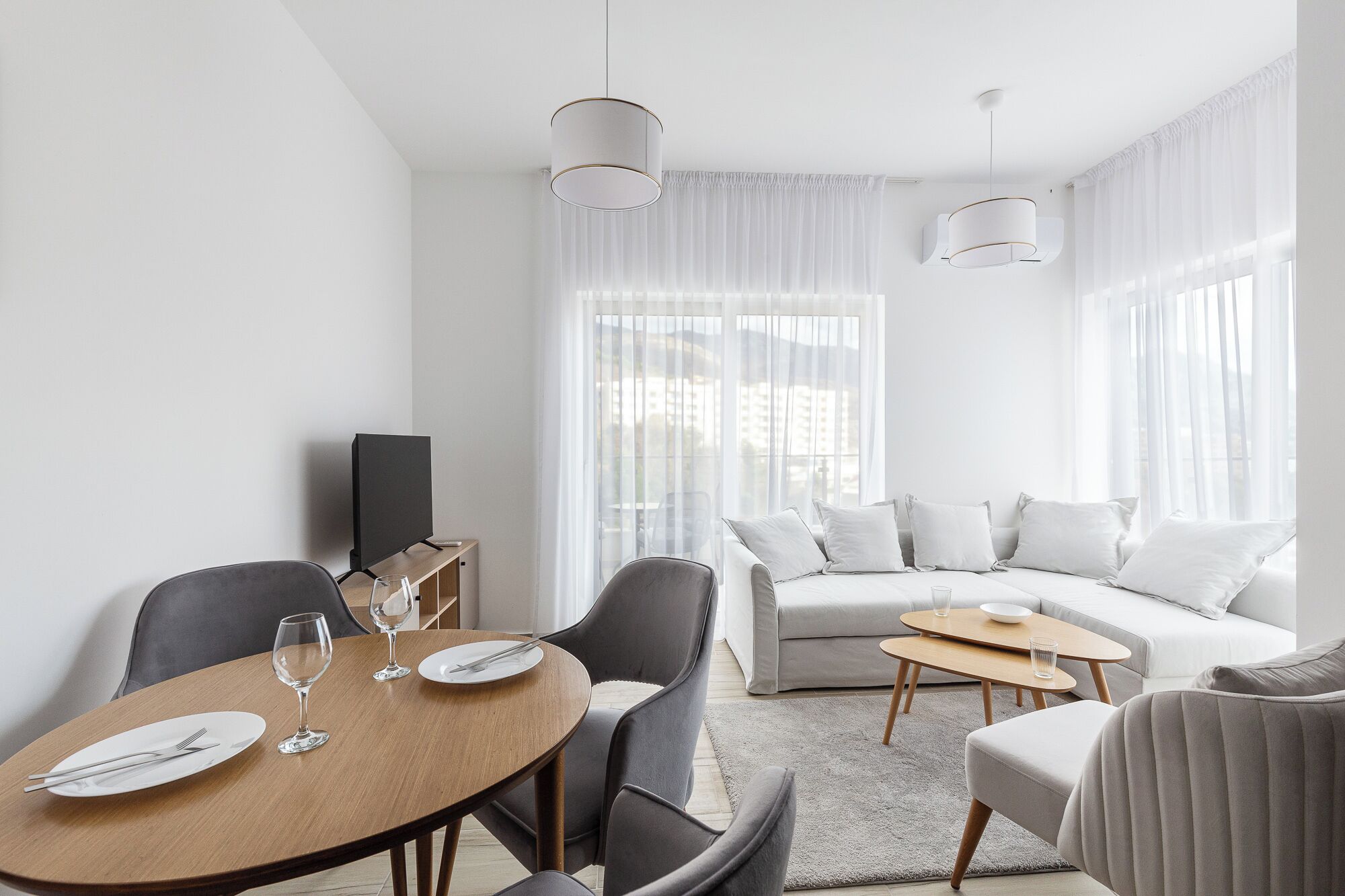 Una sala de estar moderna con comedor, que incluye un sofá, sillas, una mesa de centro y un televisor.