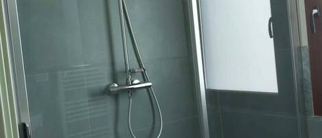 Una ducha con cerramiento de vidrio, un cabezal de ducha manual y un grifo empotrado en la pared.